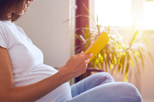 Mulher grávida leitura livro sentado no sofá — Fotografia de Stock