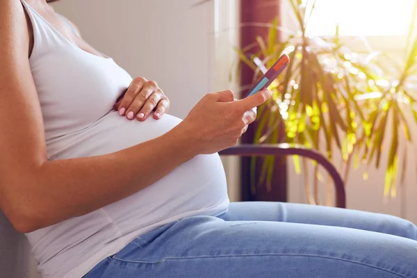 Έγκυος γυναίκα χρησιμοποιώντας τηλέφωνο στον καναπέ — Φωτογραφία Αρχείου