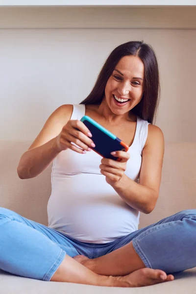 Glad gravid kvinna som spelar på telefonen hemma — Stockfoto