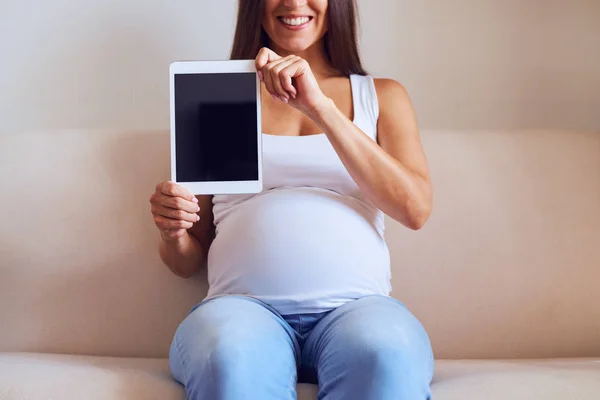 Беременная женщина держит планшет с черным экраном, сидя на — стоковое фото