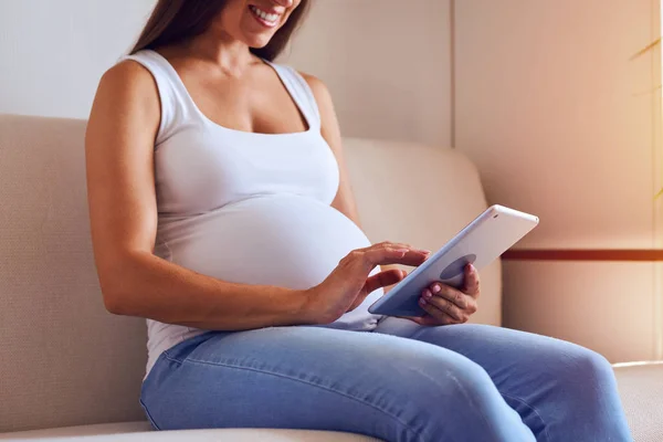 Mujer embarazada usando tableta digital en el sofá — Foto de Stock