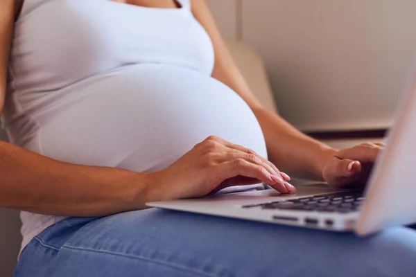 Händerna på gravid kvinna att skriva på laptop hemma — Stockfoto