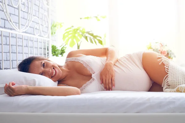Femme enceinte souriante couchée sur le côté sur le lit Images De Stock Libres De Droits