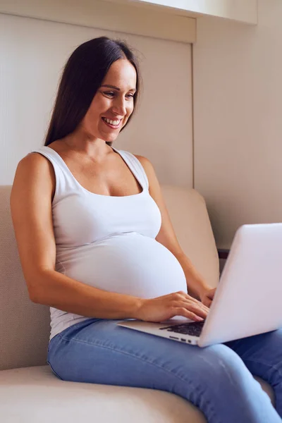 美丽的年轻孕妇与笔记本电脑坐在沙发上在浩 — 图库照片