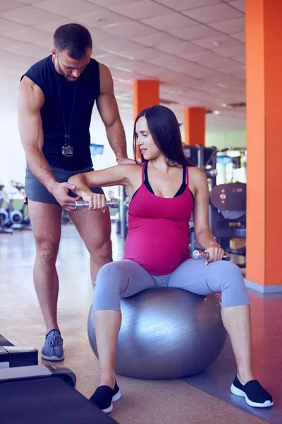 Zwangere vrouw uit te oefenen met personal trainer in de sportschool — Stockfoto