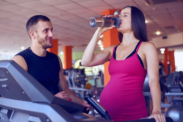 Mujer embarazada bebiendo agua mientras corre en la cinta de correr — Foto de Stock