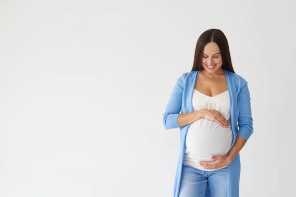 Mulher grávida tocando amorosamente barriga contra fundo branco — Fotografia de Stock