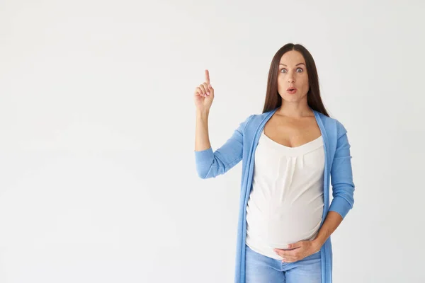 Surprised pregnant woman pointing finger up in studio — Stock Photo, Image