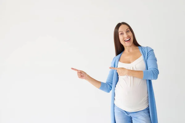 Mujer embarazada sonriente apuntando hacia un lado con los dedos —  Fotos de Stock