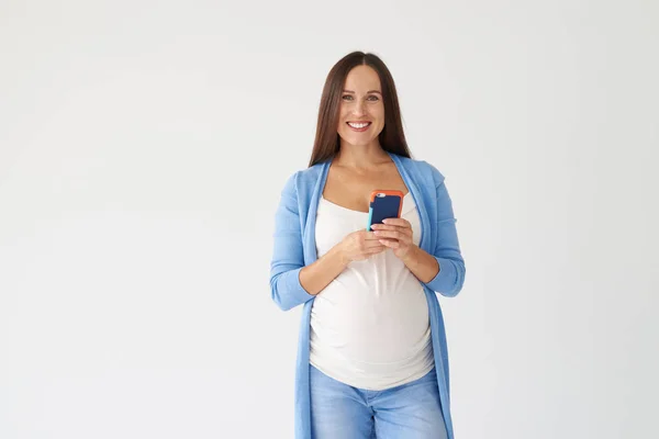 Gravid kvinna poserar med telefon mot vit bakgrund — Stockfoto