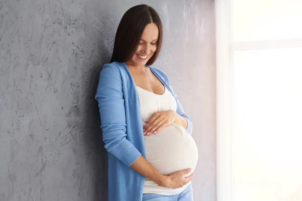 Lächelnde Schwangere blickt auf Bauch, während sie im Studio posiert — Stockfoto