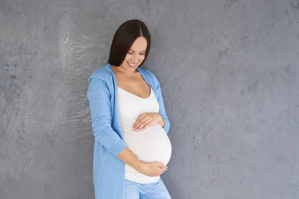 Mulher branca grávida olhando para a barriga contra backgroun cinza — Fotografia de Stock
