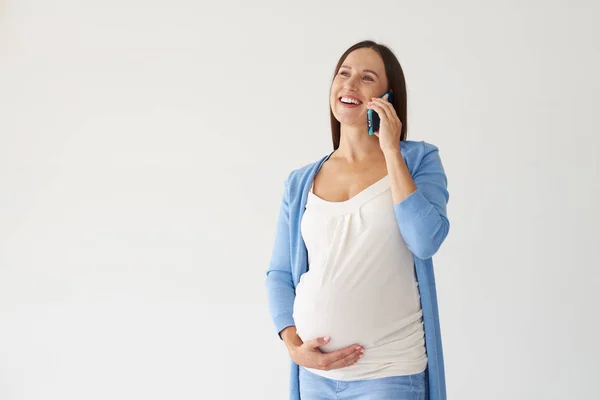 Sonriente mujer embarazada hablando en el teléfono inteligente contra respaldo blanco — Foto de Stock