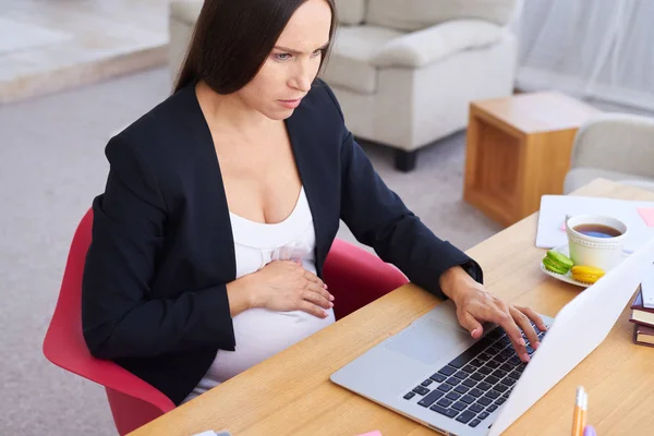 Mulher de negócios grávida concentrada usando laptop — Fotografia de Stock