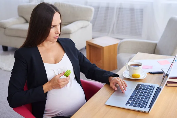 Grave mulher de negócios grávida trabalhando no laptop e comer maca — Fotografia de Stock