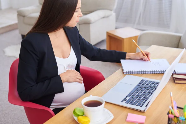 Hochschwangere Geschäftsfrau macht sich Notizen bei der Arbeit auf dem Schoß — Stockfoto