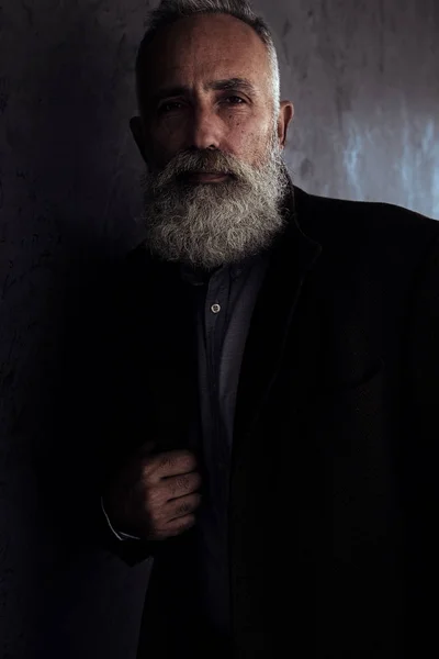 Homem sênior barbudo em casaco posando em estúdio escuro olhar de fundo — Fotografia de Stock