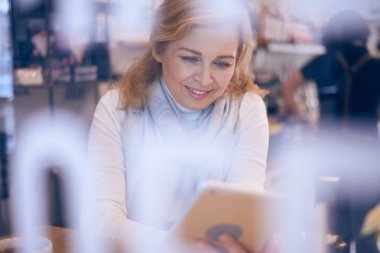 Pencere arkasından tablet üzerinde çalışan Modern Olgun kadın