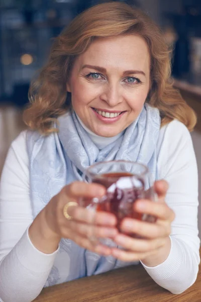 Donna sorridente che tiene una tazza di tè per riscaldarsi le mani — Foto Stock