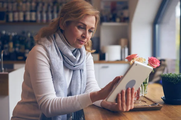 Schöne reife Frau mit Tablette, sitzt im Café — Stockfoto