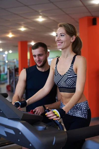 Donna sorridente che cammina sul tapis roulant con personal trainer — Foto Stock