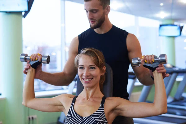 Lächelnde Frau und Personal Trainer beim Training im Fitnessstudio — Stockfoto