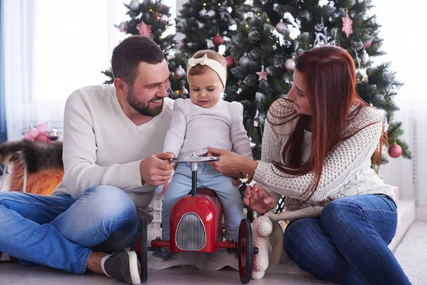 Petite fille assise sur une voiture jouet rétro avec des parents près de Chris — Photo