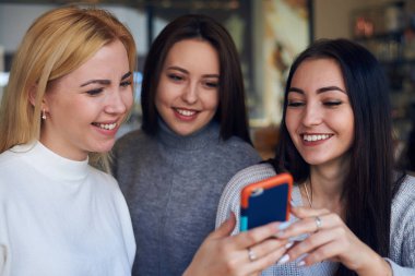 Bir şey telefonla arıyor ve gülümseyen üç kadın arkadaş