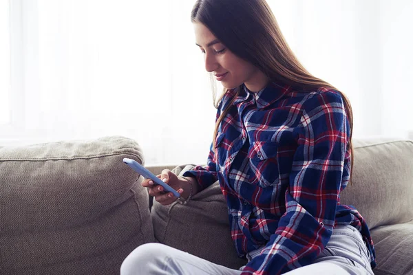 Leende flicka att skriva meddelande via telefon på soffa — Stockfoto