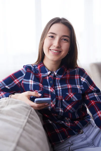 Menina agradável sentado no sofá com telefone — Fotografia de Stock