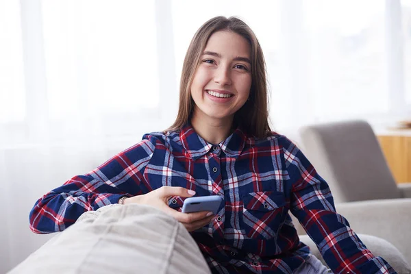 Menina feliz usando telefone no sofá em casa — Fotografia de Stock