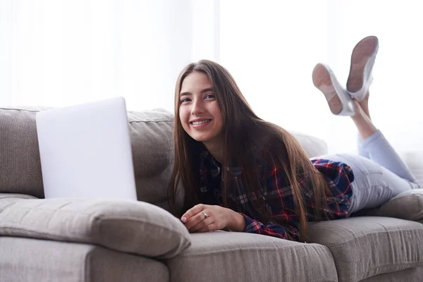 Relajada chica acostada en el sofá con el ordenador portátil —  Fotos de Stock