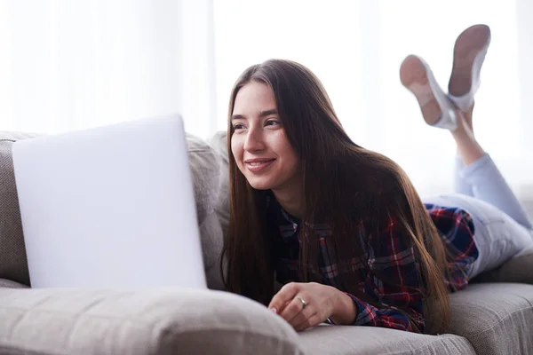 Hermosa chica relajándose con su computadora portátil mientras está acostada en el sofá — Foto de Stock