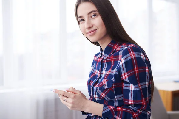 Stijlvolle meisje gelukkig glimlachen naar de camera tijdens het gebruik van de telefoon — Stockfoto