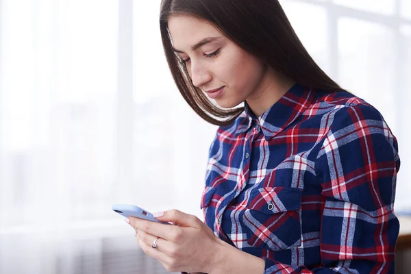 Jonge brunette meisje surfen op het net via telefoon thuis — Stockfoto