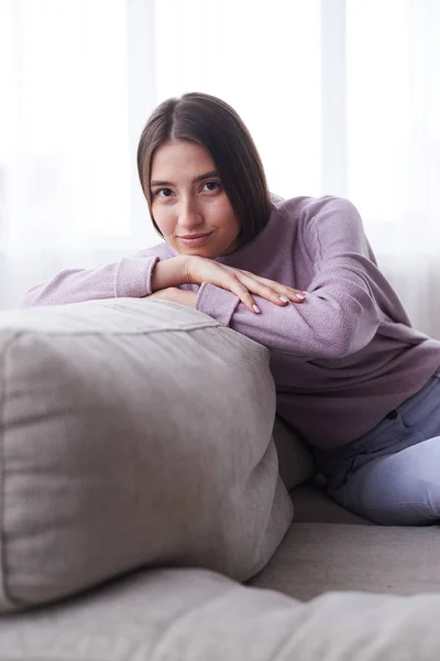 Glad ung flicka sittande på soffan i mysiga dukar — Stockfoto