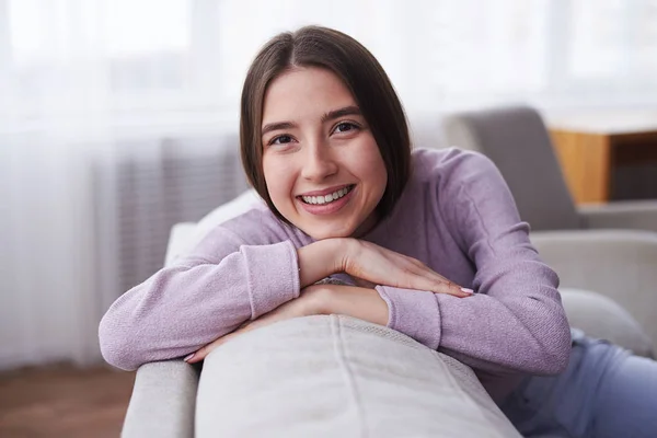 微笑俏丽的女孩在舒适的毛衣倾斜在沙发 — 图库照片