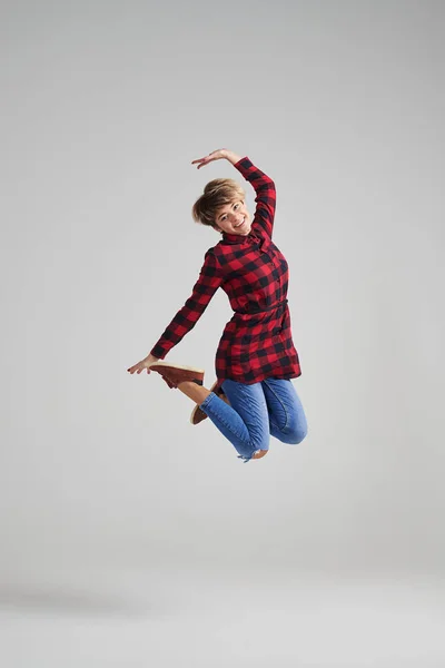 Young woman jumping in the air happily at studio — Stock Photo, Image