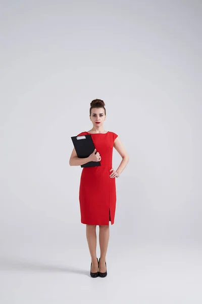 Szigorú fiatal üzletasszony, piros ruhás gazdaság mappában — Stock Fotó