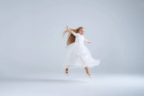 Menina pequena vestindo vestido branco saltando no estúdio — Fotografia de Stock