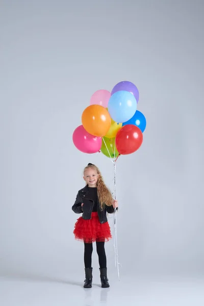 Joyful girl in rock style outfit holding colorful balloons