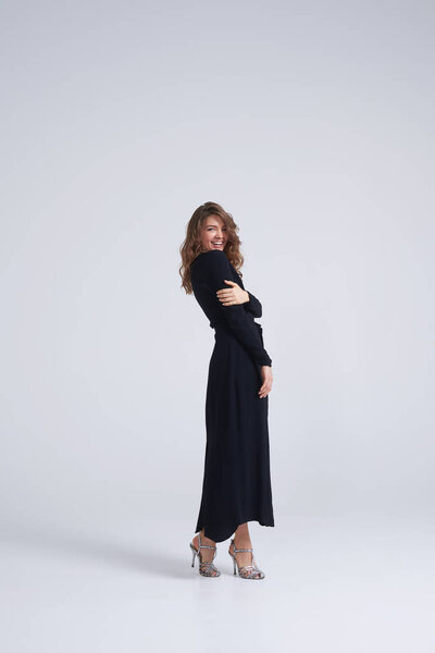 Чувственная брюнетка в черном платье смотрит через плечо
