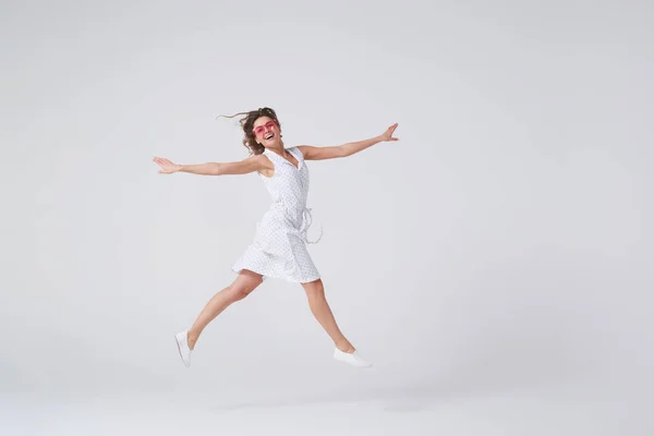 Chica juguetona haciendo gestos y sonriendo mientras salta contra el backgro — Foto de Stock