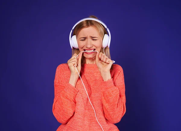 Chateado mulher em fones de ouvido mordendo cordão — Fotografia de Stock