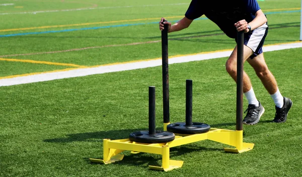 Athlete pushing a sled with weights on a turf field — Stock Photo, Image