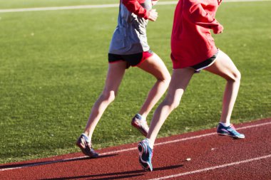 Two girls running together on a track clipart