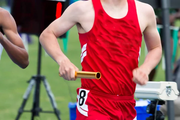 High school runner racing ett relä med en batong — Stockfoto