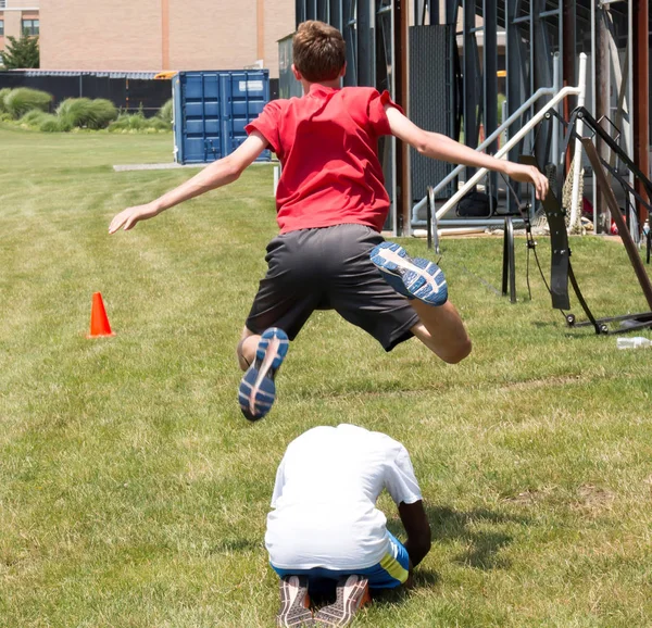 Leapfrogging your teammate on the grass behind the bleaches — Stock Photo, Image