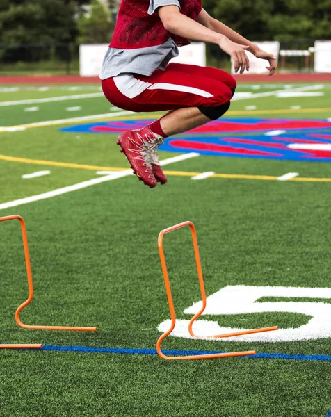 Gymnasiet fotbollsspelare bounding över häck — Stockfoto
