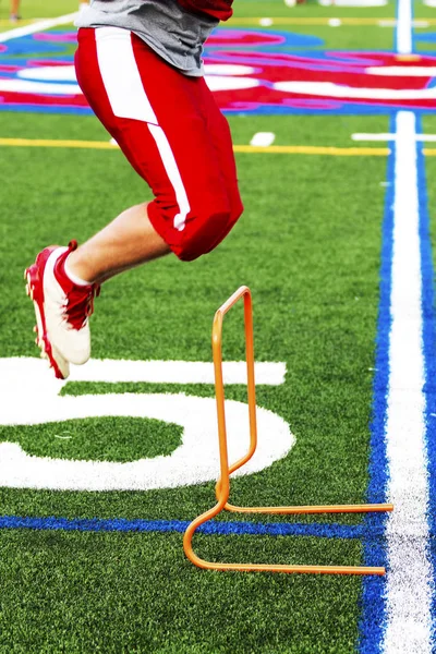 Jogador de futebol do ensino médio saltando obstáculos na prática — Fotografia de Stock